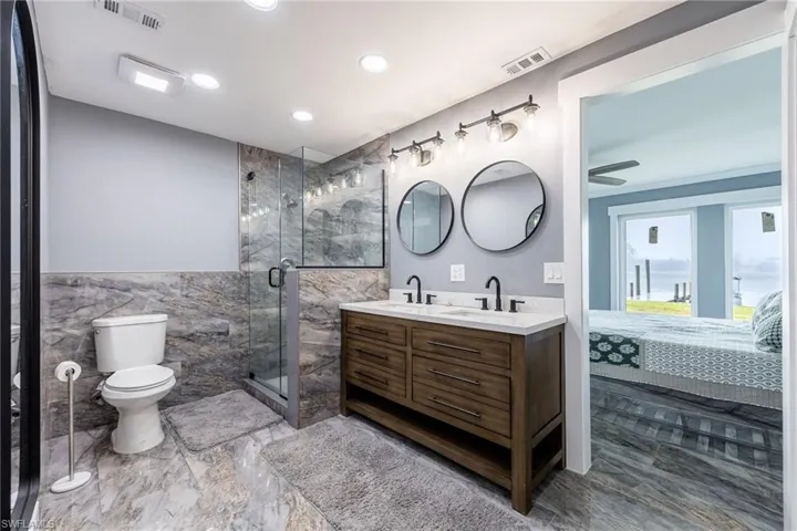 Ensuite bathroom featuring double vanity, a marble finish shower, tile walls, recessed lighting, and wainscoting