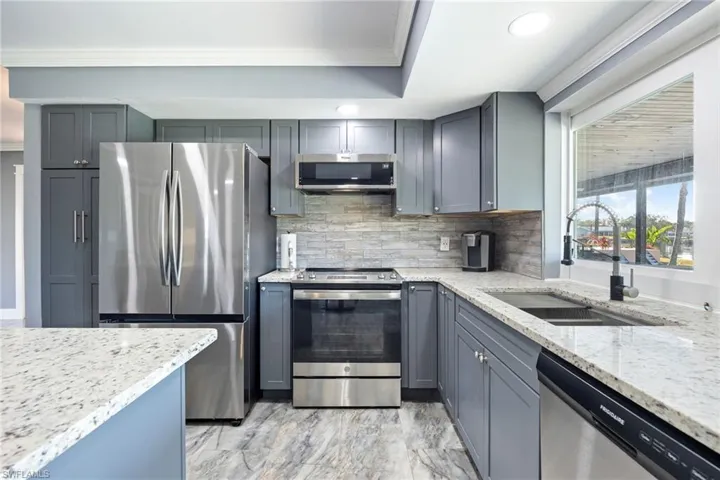 Kitchen featuring stainless steel appliances, light stone countertops, crown molding, gray cabinetry, and decorative backsplash