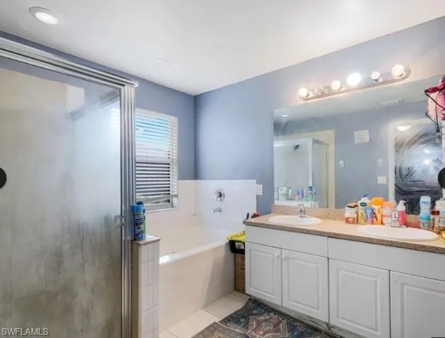 Bathroom featuring a glass-enclosed shower, built-in soaking tub, dual vanity with undermount sinks, and a framed mirror
