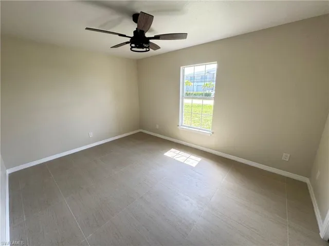 Room featuring light-toned walls, tile flooring, and a ceiling fan with wood-finish blades