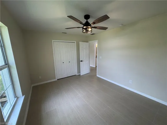 Neutral-toned room featuring a ceiling fan with integrated lighting, a large window, tiled flooring, and a bi-fold closet door