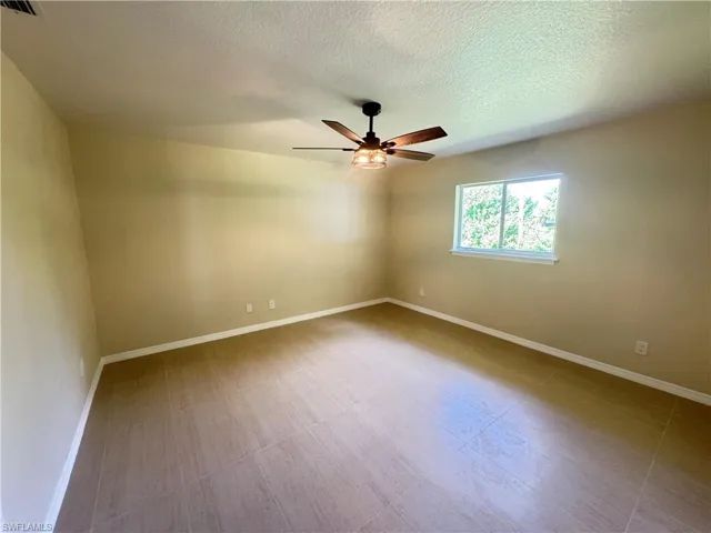 Spacious room featuring neutral wall tones, large format tile flooring, a ceiling fan with light fixture, and a window providing natural illumination