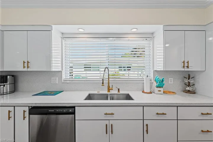 Kitchen featuring stainless steel dishwasher, ornamental molding, white cabinetry, light countertops, and backsplash