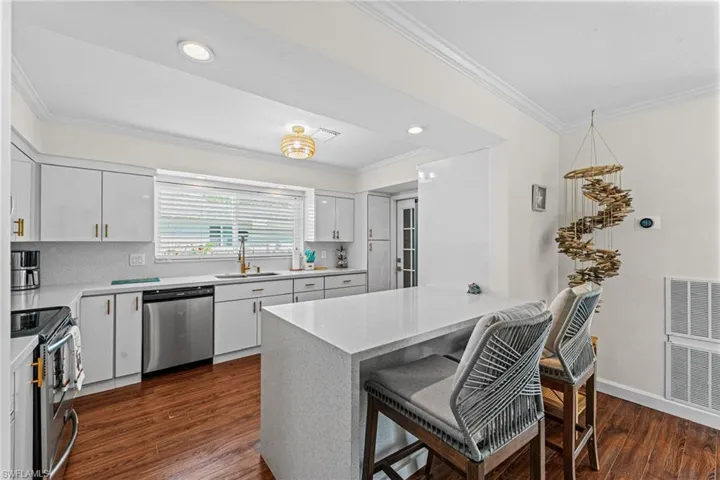 Kitchen with appliances with stainless steel finishes, ornamental molding, dark wood-style floors, a kitchen bar, and decorative backsplash