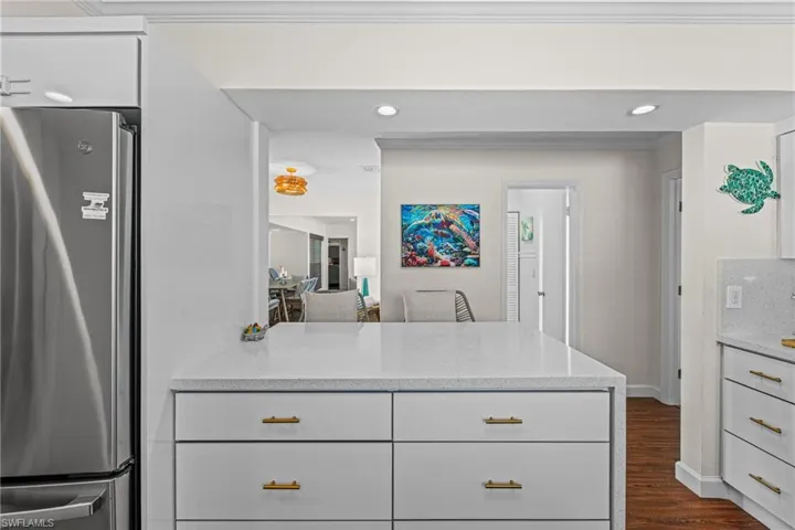 Kitchen featuring freestanding refrigerator, light stone countertops, white cabinets, dark wood finished floors, and a peninsula