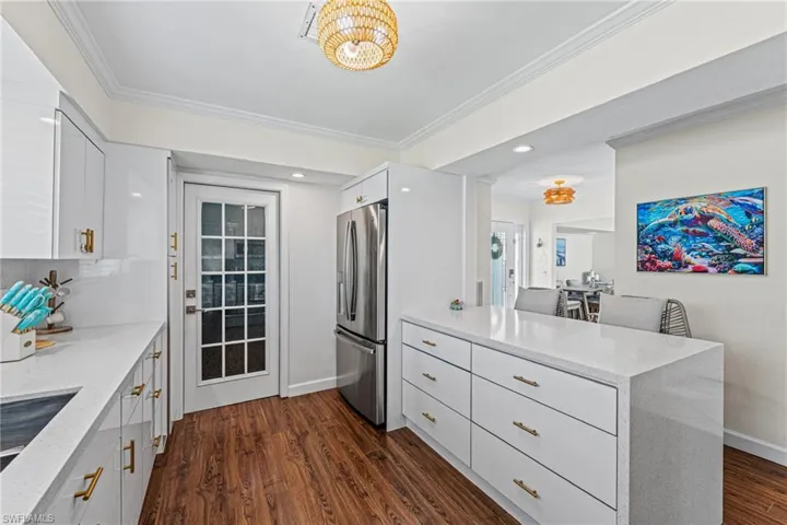 Kitchen with stainless steel fridge with ice dispenser, a peninsula, ornamental molding, light stone counters, and white cabinetry