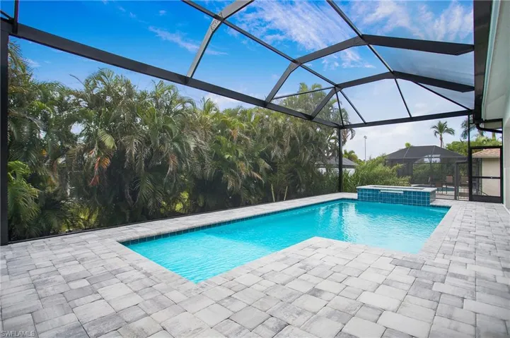 View of swimming pool featuring glass enclosure, a patio, and an in ground hot tub