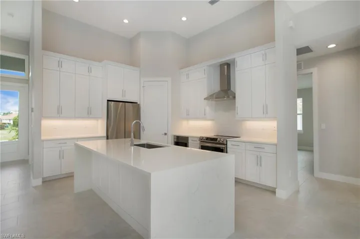Kitchen featuring wall chimney exhaust hood, sink, an island with sink, white cabinetry, and appliances with stainless steel finishes