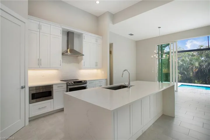 Kitchen featuring a center island with sink, sink, appliances with stainless steel finishes, wall chimney exhaust hood, and white cabinets
