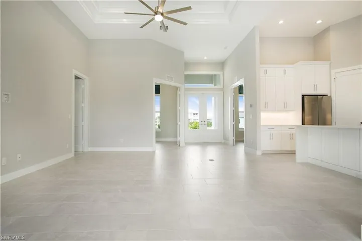 Unfurnished living room with a high ceiling, ceiling fan, light tile patterned floors, and ornamental molding