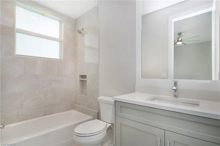 Full bathroom with vanity, ceiling fan, tiled shower / bath, and toilet