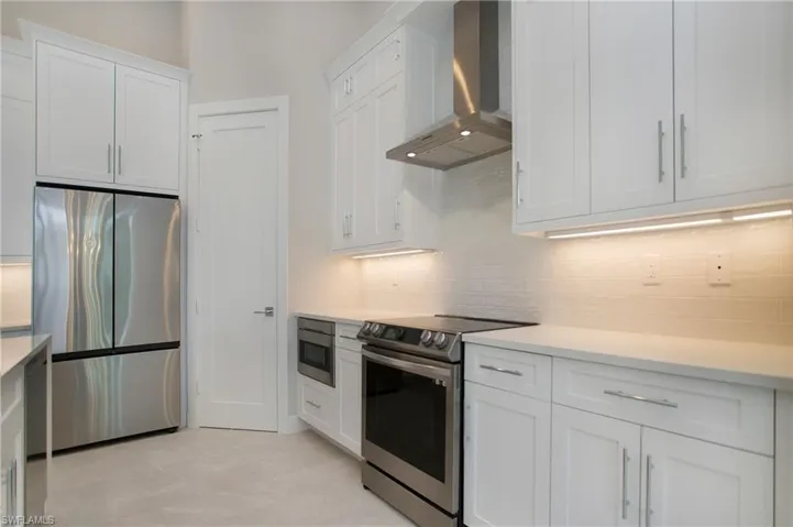 Kitchen featuring white cabinetry, appliances with stainless steel finishes, wall chimney range hood, and backsplash