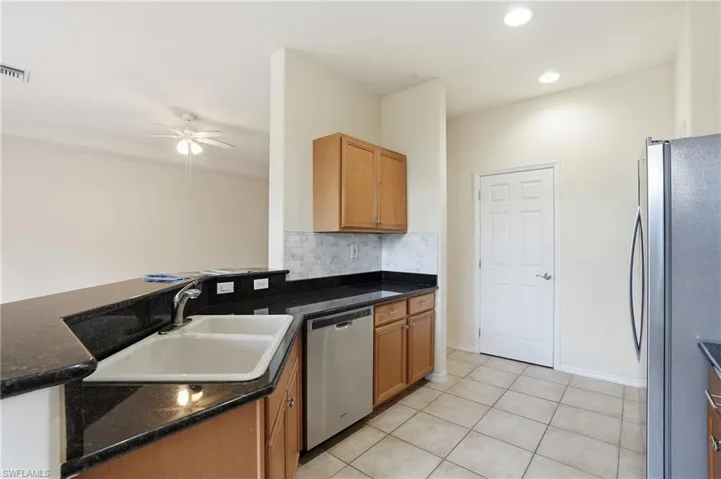 Kitchen with stainless steel appliances, decorative backsplash, a ceiling fan, light tile patterned floors, and dark stone counters