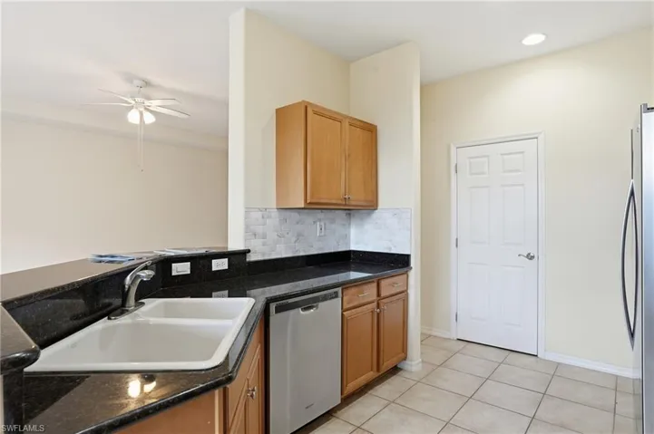 Kitchen with stainless steel appliances, ceiling fan, backsplash, light tile patterned floors, and dark stone countertops
