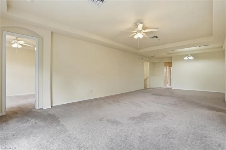 Empty room with a ceiling fan, a tray ceiling, and light colored carpet