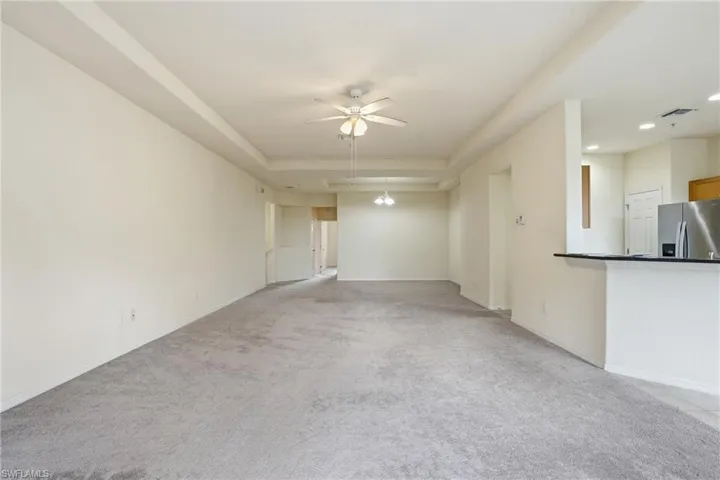 Unfurnished living room featuring ceiling fan, light colored carpet, a raised ceiling, and recessed lighting