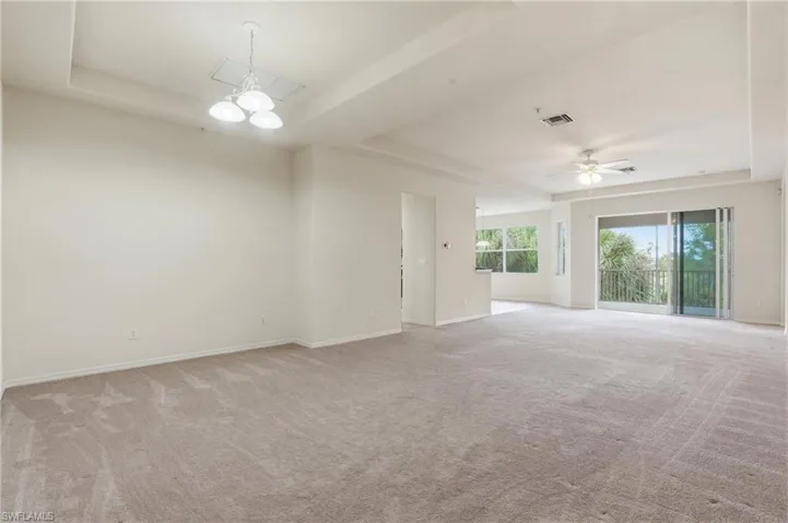 Unfurnished room featuring a raised ceiling, light carpet, and a ceiling fan