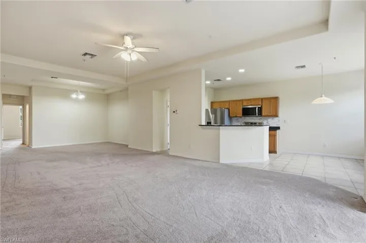 Unfurnished living room featuring a raised ceiling, ceiling fan, light carpet, and recessed lighting