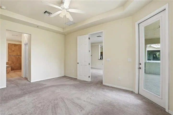 Unfurnished bedroom with a raised ceiling, light carpet, ceiling fan, and ensuite bathroom