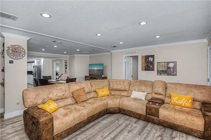 Living area with crown molding, light wood-style flooring, a textured ceiling, and recessed lighting