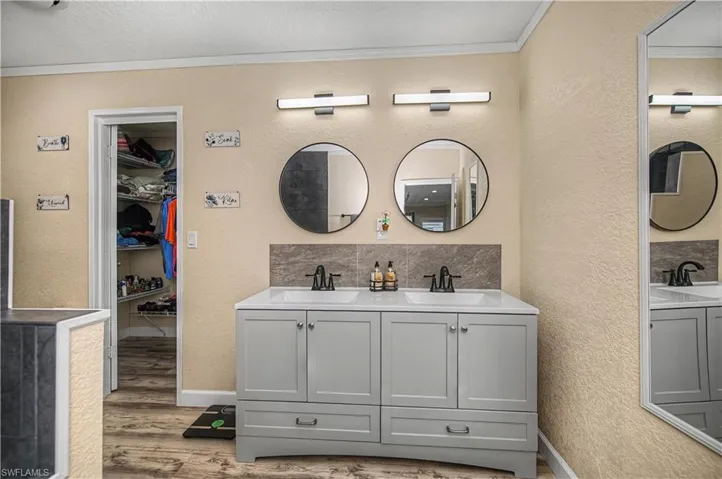 Full bath with double vanity, a textured wall, crown molding, a spacious closet, and light wood-style floors
