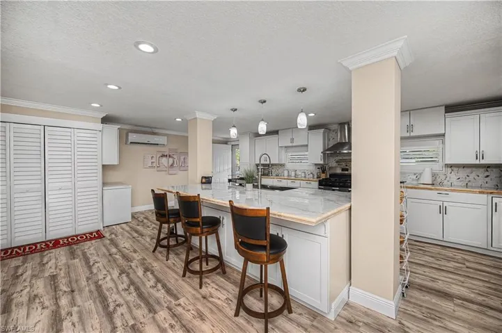 Kitchen with light wood-style floors, a breakfast bar, hanging light fixtures, crown molding, and white cabinets