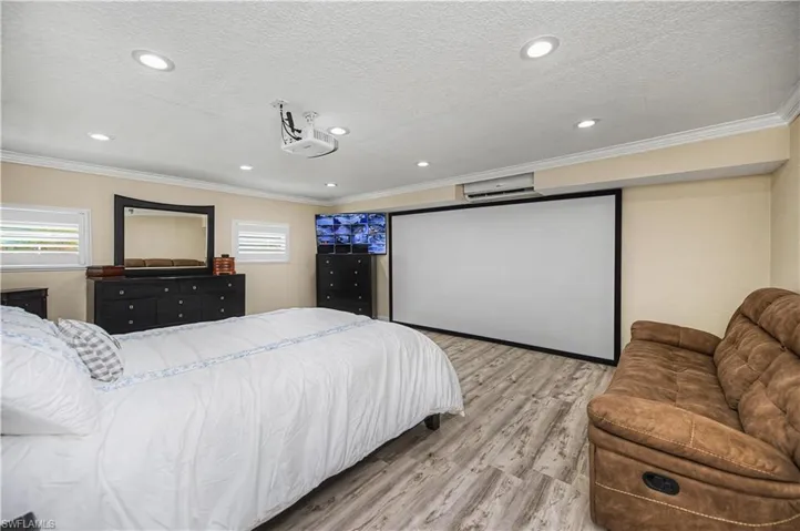 Bedroom featuring light wood-style floors, a textured ceiling, ornamental molding, a wall unit AC, and recessed lighting