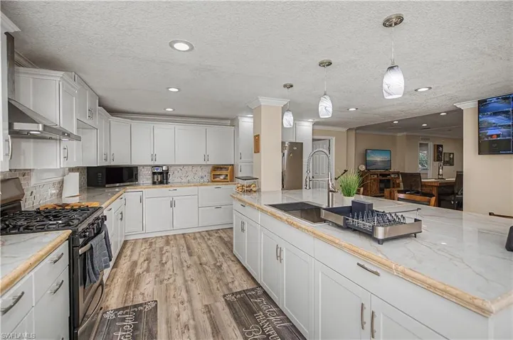 Kitchen featuring appliances with stainless steel finishes, white cabinetry, pendant lighting, backsplash, and a textured ceiling