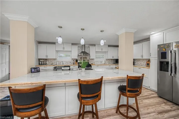 Kitchen with a kitchen breakfast bar, stainless steel refrigerator with ice dispenser, pendant lighting, white cabinets, and ornamental molding