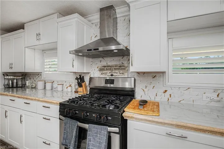 Kitchen featuring stainless steel gas stove, wall chimney range hood, white cabinetry, tasteful backsplash, and a textured ceiling