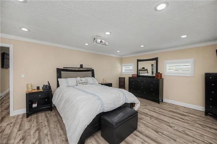 Bedroom with light wood-style floors, multiple windows, a textured ceiling, recessed lighting, and ornamental molding