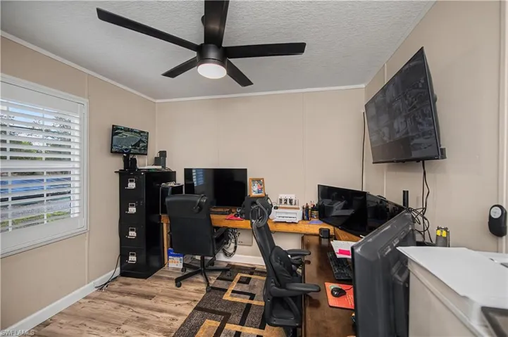 Office featuring a textured ceiling, light wood finished floors, a decorative wall, ceiling fan, and crown molding