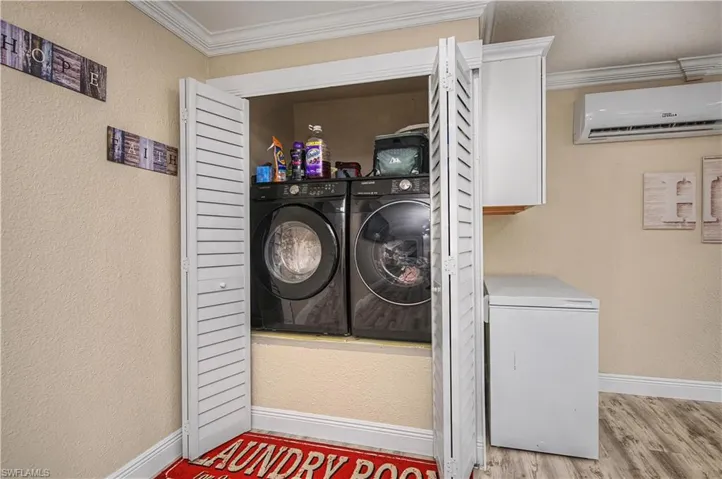 Laundry room with a textured wall, crown molding, a wall mounted AC, light wood finished floors, and washer and clothes dryer