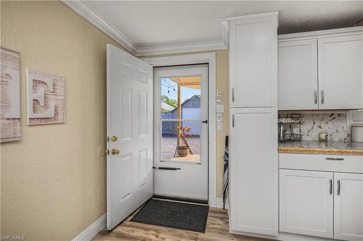 Doorway to outside with wood finished floors, a textured wall, and crown molding