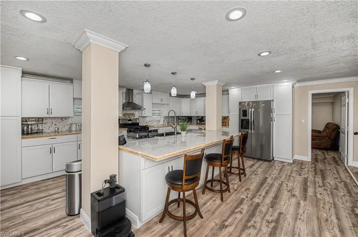 Kitchen with stainless steel appliances, pendant lighting, white cabinets, light wood-style floors, and a kitchen bar