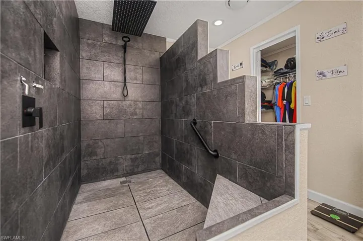 Full bath with a tile shower, a spacious closet, pet washing station, a textured ceiling, and a textured wall
