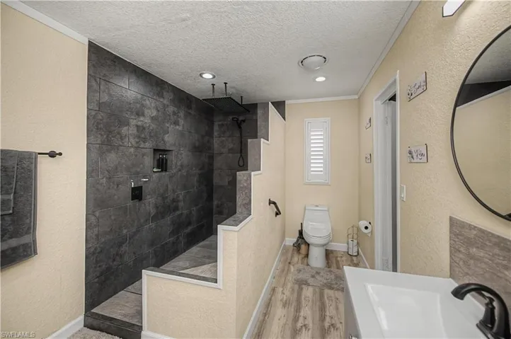 Full bathroom featuring walk in shower, a textured ceiling, crown molding, light wood-type flooring, and a textured wall
