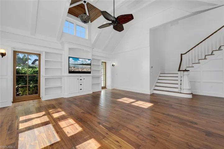 Unfurnished living room featuring ceiling fan, built in shelves, dark wood-type flooring, and a high ceiling
