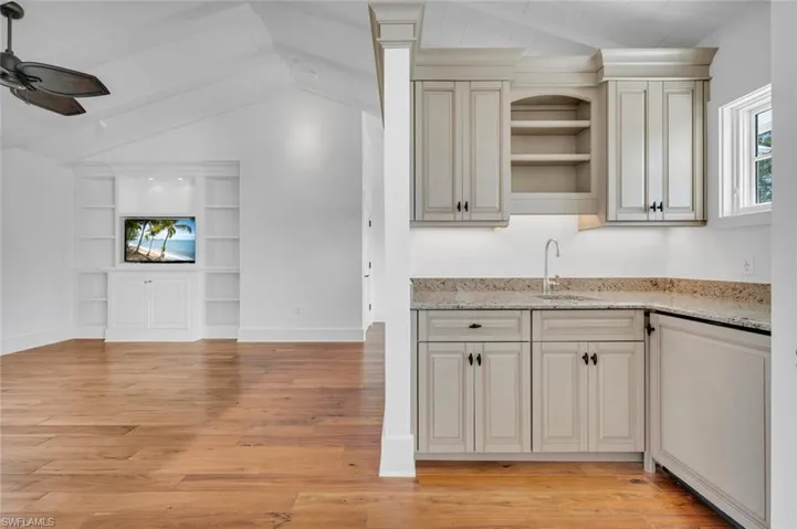Kitchen with light hardwood / wood-style floors, ceiling fan, vaulted ceiling with beams, light stone countertops, and sink
