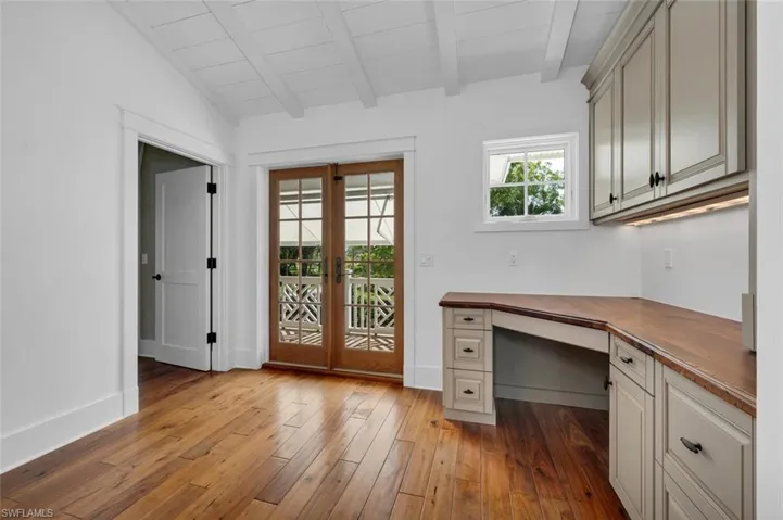 Unfurnished office with light hardwood / wood-style floors, built in desk, lofted ceiling with beams, wood ceiling, and french doors