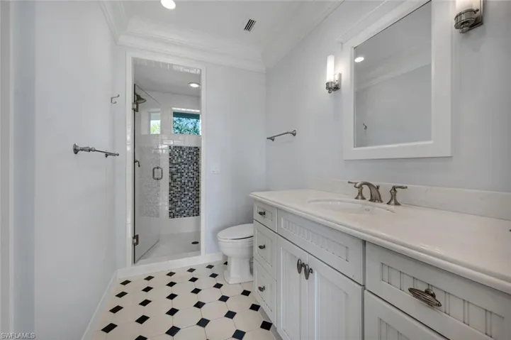 Bathroom featuring a shower with shower door, toilet, vanity, and crown molding