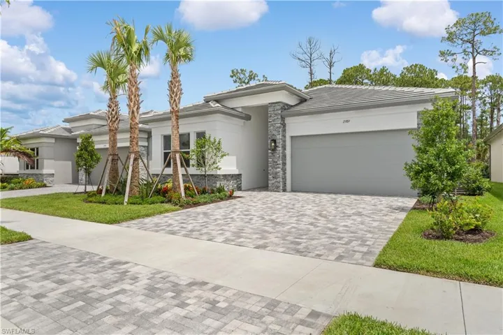 A crisp, new-construction home featuring a modern blend of stone and stucco siding, tile roof, an attached two-car garage with a stone driveway, and manicured tropical landscaping