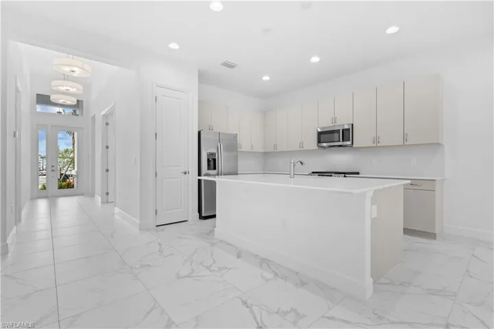 A stylish, modern kitchen equipped with premium stainless steel appliances, a large central island with a breakfast bar, beautiful cabinetry, natural gas cooking, and a pantry