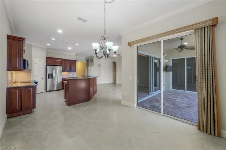 Kitchen with ceiling fan with notable chandelier, stainless steel refrigerator with ice dispenser, tasteful backsplash, decorative light fixtures, and a kitchen island
