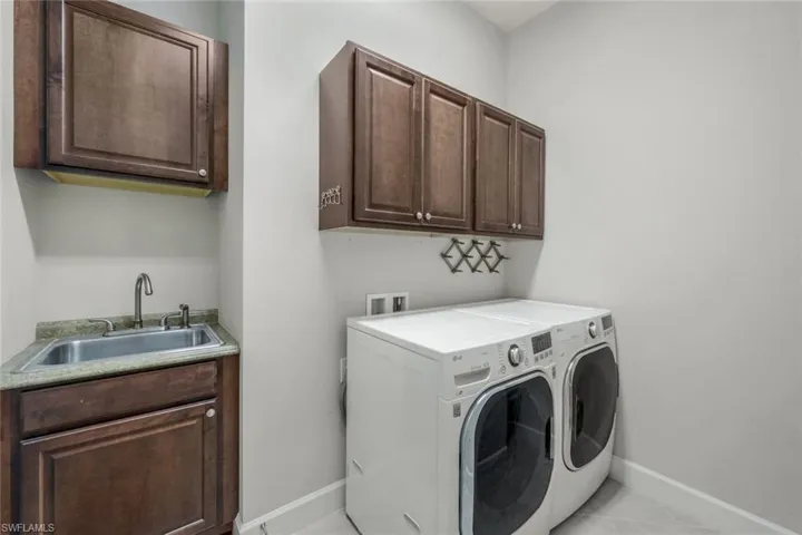 Washroom with light tile patterned flooring, cabinets, independent washer and dryer, and sink