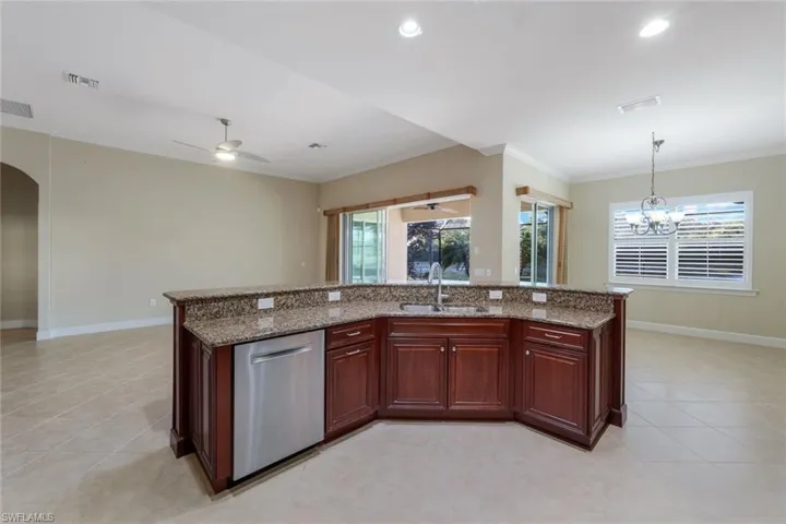 Kitchen with dishwasher, ceiling fan with notable chandelier, crown molding, sink, and light stone counters