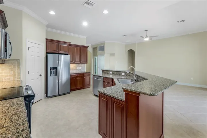 Kitchen featuring ceiling fan, sink, tasteful backsplash, a kitchen island with sink, and appliances with stainless steel finishes