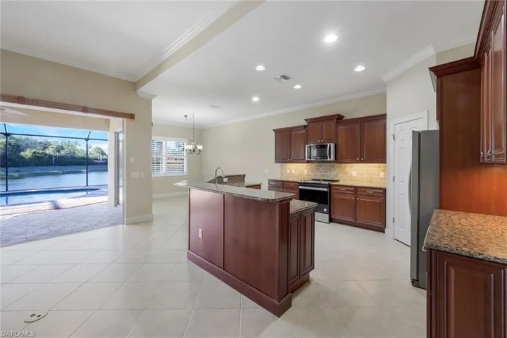 Kitchen with a center island with sink, crown molding, light stone countertops, appliances with stainless steel finishes, and decorative light fixtures
