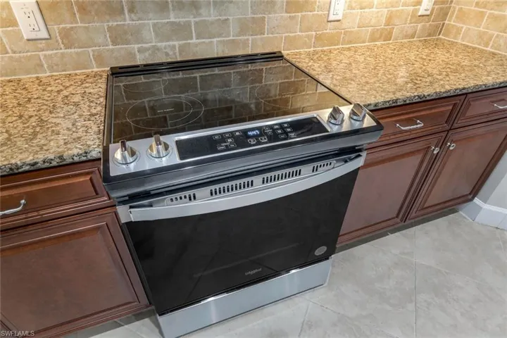 Kitchen with stainless steel electric range, light stone counters, light tile patterned floors, and backsplash