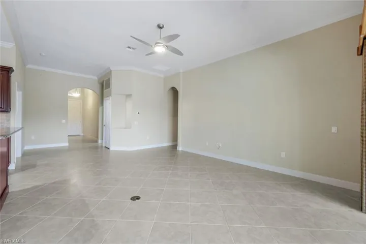 Unfurnished living room with light tile patterned floors, ceiling fan, and crown molding